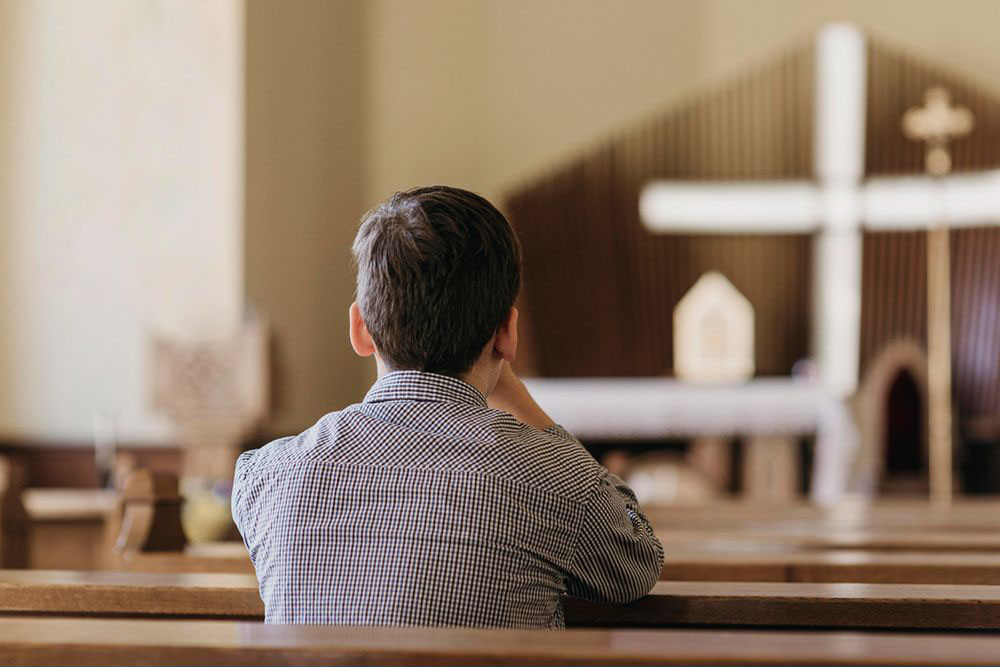 Back view young boy praying in the church