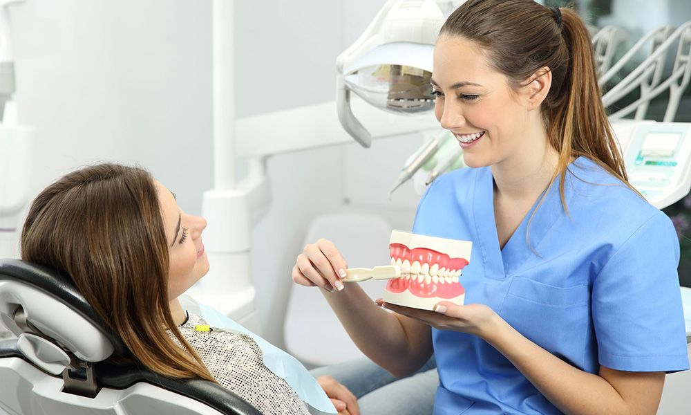 Dental hygienist shows patient how to brush her teeth