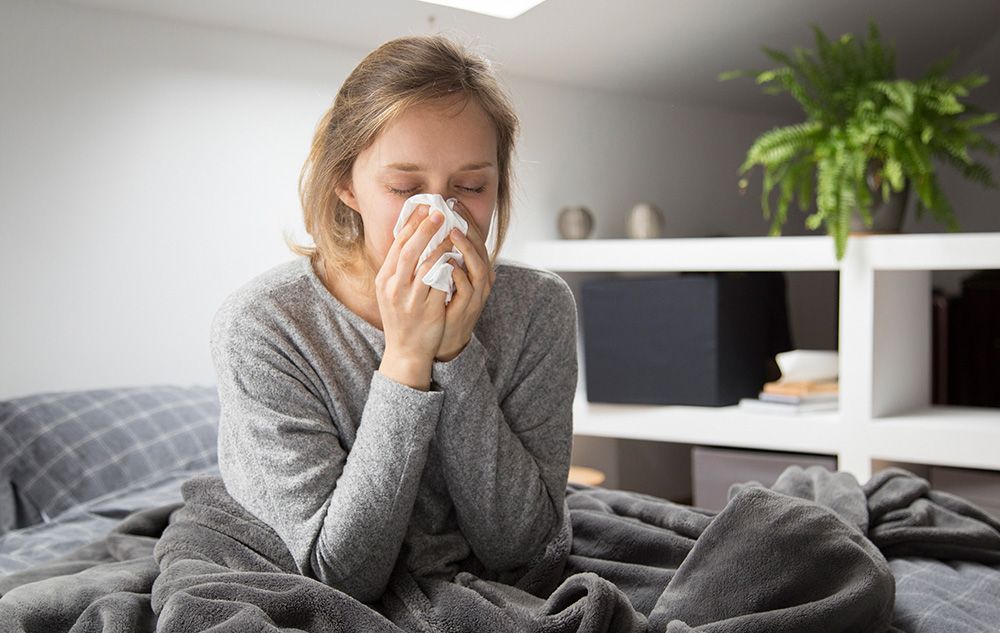 Sick woman sitting in bed blowing nose with napkin