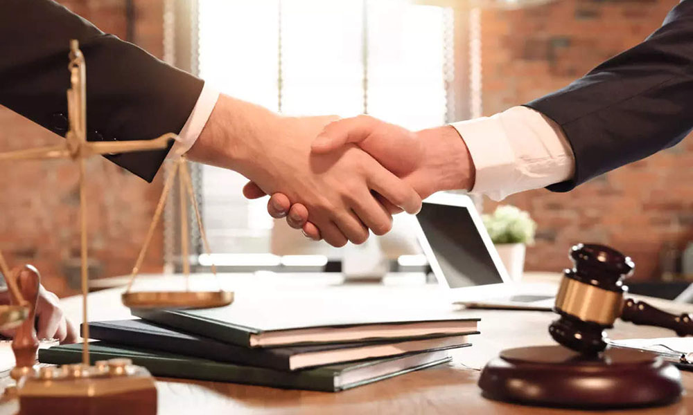Two people shake hands over a desk with legal paraphernalia